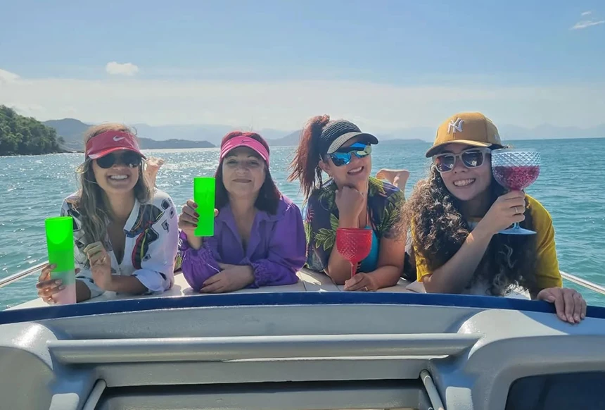 Grupo de amigas deitadas na proa de lancha, fazendo um brinde, em despedida de solteira.
