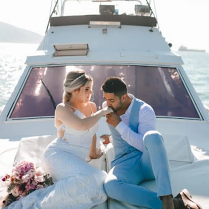 Pedido de caamento a bordo. Ela vestida de noiva. O casal está sentado na proa da lancha. Ele beija a mão dela.